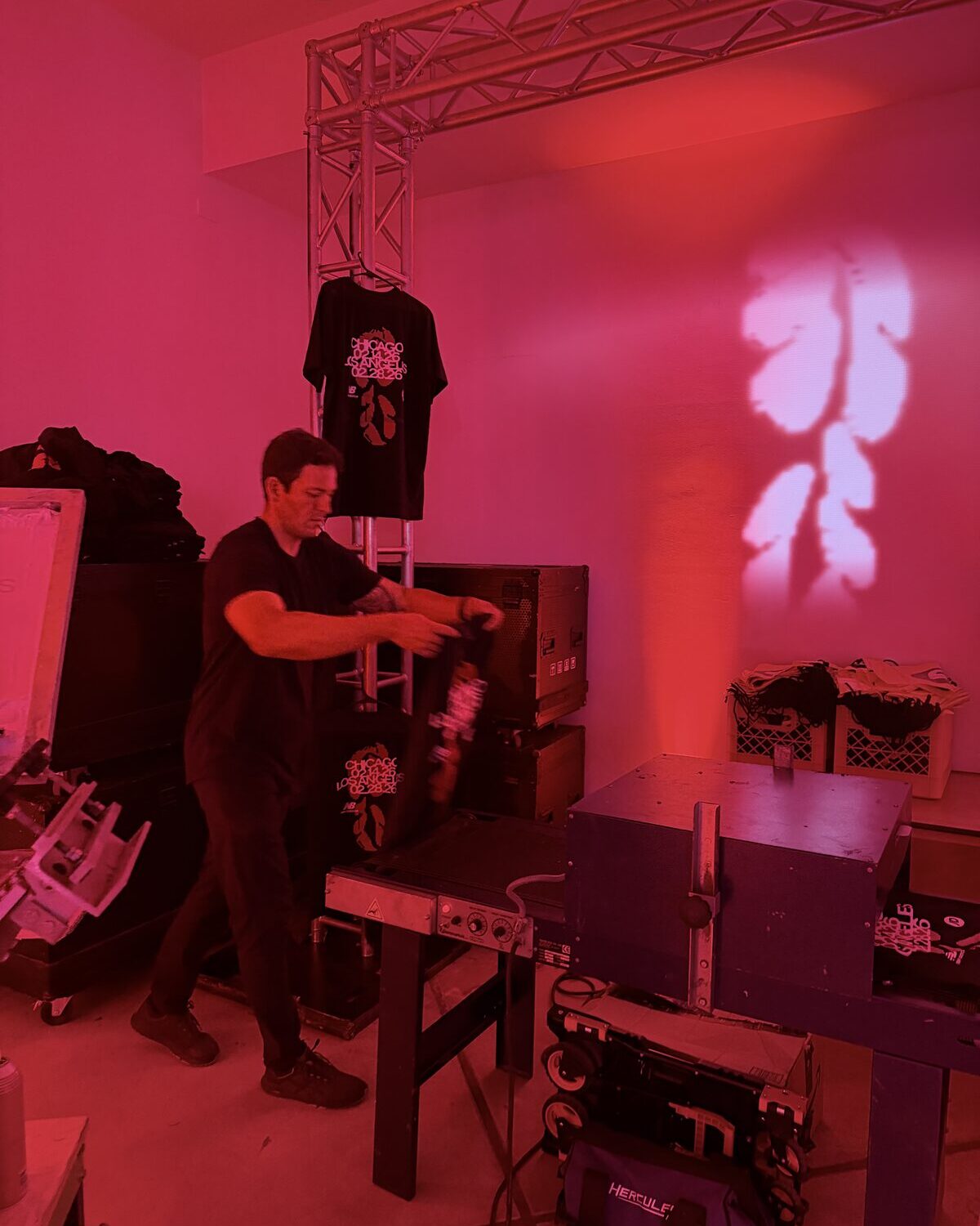 Backstage print and press setup with truss rigging and event shirts hung overhead