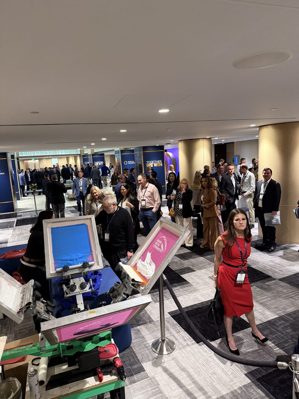 Conference attendees gathering around a live shirt printing line in a hotel corridor