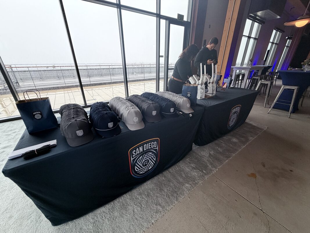 Merch table with rows of custom hats and cap presses at a soccer club event